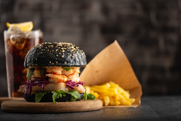 Black burger with fish and shrimps. Fishburger with prawns and French Fries