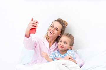 smiling mother and daughter taking selfie with smartphone on bed at home