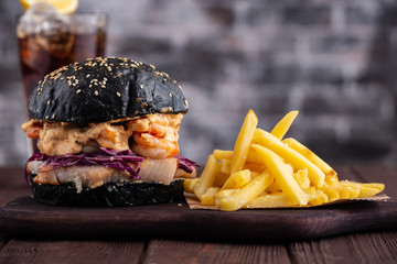Black burger with fish and shrimps. Fishburger with prawns and French Fries