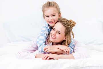 happy daughter hugging mother on bed at home