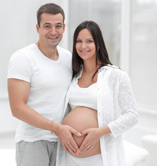 husband and pregnant wife with folded hands in the shape of a heart on his tummy