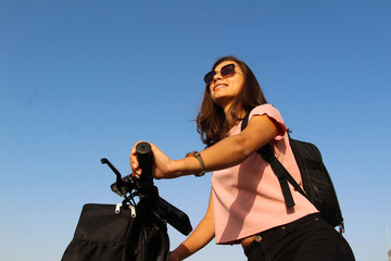 A young smiling woman on an bicycle with Backpack and sunglasses at a background of sky