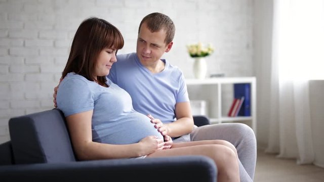 pregnant woman and her husband sitting on a sofa and touching pregnant tummy
