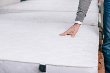 cropped shot of man choosing mattress in furniture store