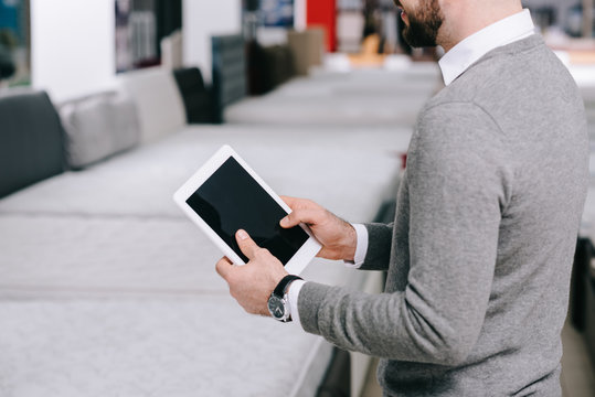 Cropped Shot Of Man Using Digital Tablet With Blank Screen In Furniture Store With Arranged Mattresses