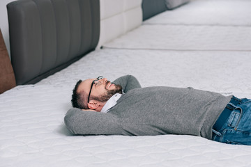 side view of smiling customer lying on orthopedic mattress in furniture store
