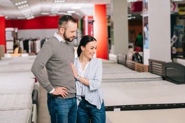 side view of couple choosing mattress together in furniture shop