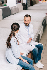 Obraz premium shop assistant in white coat and female customer in furniture store with arranged mattresses