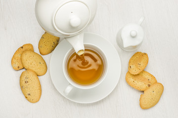 pouring tea into cup on white table with cookies and milk jug