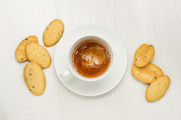 cup with splashing tea on white table with cookies
