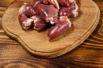 Raw chicken hearts on cutting board on wooden table
