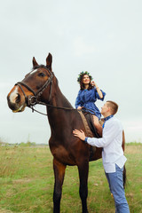happy girl is sitting on a horse and her boyfriend stands next to her looking at her