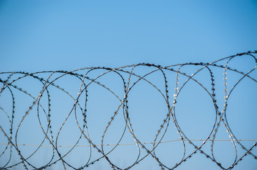 Close up view of security camera hanging among barbwire in prison or other guarded object with blue sky background. Modern ways of supervision. Using new technology in security and safety.