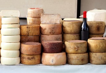Cheese wheels of Pecorino and Sardinian ricotta in different stacks on a shelf of an outdoor market. A bottle of red wine Cannonau in the middle