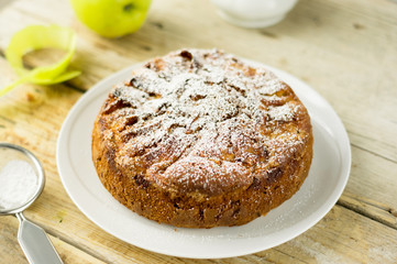 HOMEMADE RUSTIC APPLE CAKE PIE POWDERED WITH SUGAR ON A WHITE PLATE ON A WOODEN TABLE