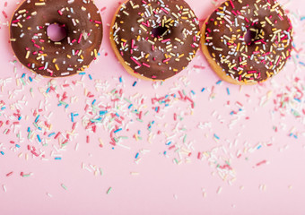 chocolate donuts with colorful sprinkles on pink background