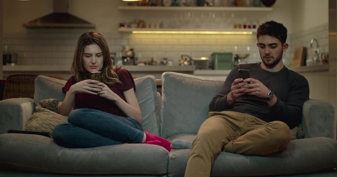 Married couple sitting on a sofa using their smart phones