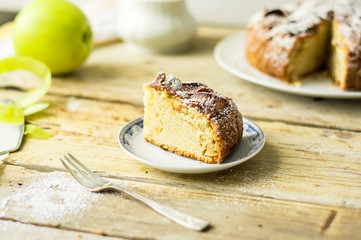 2. Piece of a freshly baked homemade apple pie with cake, fresh apple, silver fork and a powdered sugar on a side
