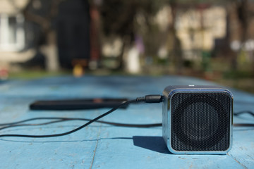 Gadgets concept with music loud speaker and unfocused black phone on blue table background texture