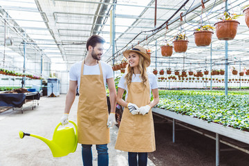 Gardeners with rake and watering can walking among plants in glasshouse