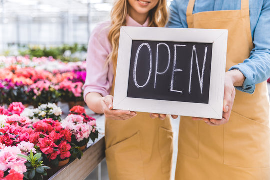 Close-up view of Open board in hands of owners of greenhouse standing among flowers