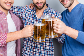 Close up cropped portrait of cheerful, stylish, half face men clinking big glasses with beer, having fun, spending time together, isolated on grey background