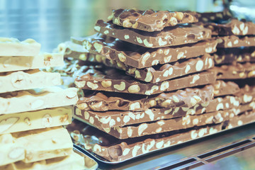 Closeup stack of assortment luxury handmade chocolate, dark and white chocolate bars with nuts in shop window.