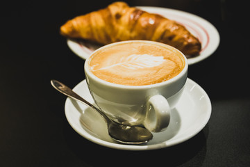Coffee relax time. Cappuccino with croissant on black background.