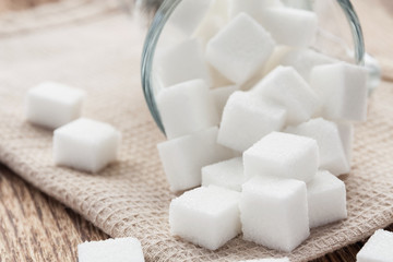 Cubes of white sugar in a glass cup and on the beige towel. Closeup, selective focus
