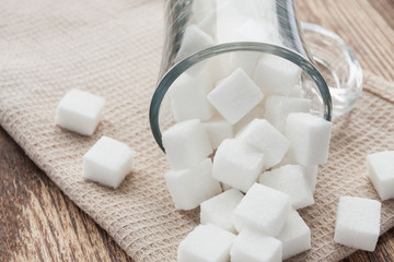 Cubes of white sugar in a glass cup and on the beige towel. Closeup, selective focus