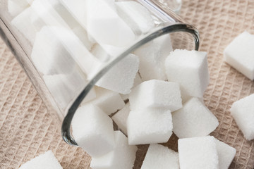 Cubes of white sugar in a glass cup and on the beige towel. Closeup, selective focus