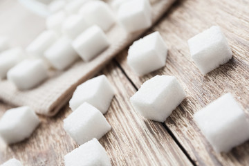 Cubes of white sugar on the wooden surface and on the beige towel. Closeup, selective focus