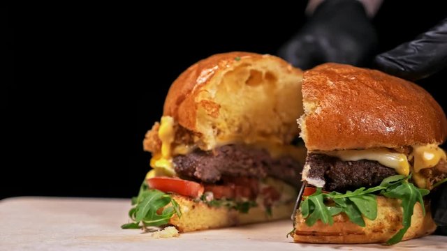 Burger is cooking on black background in black food gloves. Very luscious air bun and marbled beef. Restaurant where each burgers is cooked by hand. Burger cut on the table with a knife. Not made