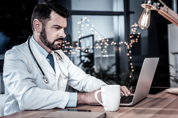 Modern medicine. Serious occupied unshaken doctor sitting in his cabinet concentrating his...