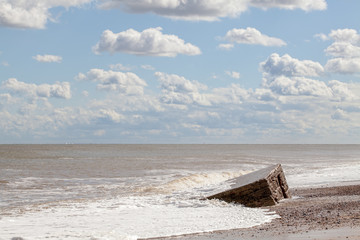 Coastal erosion and flooding. Pretty coastal landscape with clouds and partially buried WW2 beach...