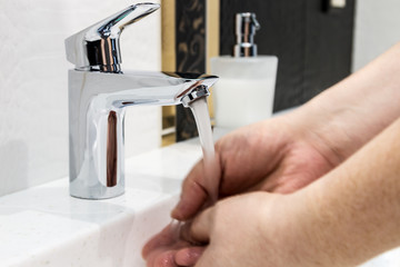 water faucet in the bathroom or toilet. water flows from the tap into male hands. Hands blurred