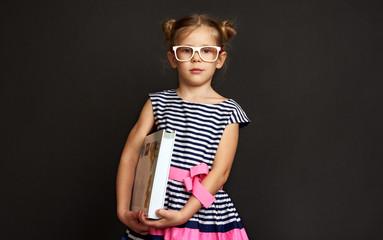Smart child holding big book over black background. Concept of knowledge and education. 