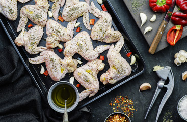 Preparing food with raw organic chicken wings placed with fresh ingredients on black tray. Top view with close-up