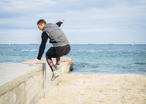Young man doing parkour tricks on the beach near the sea