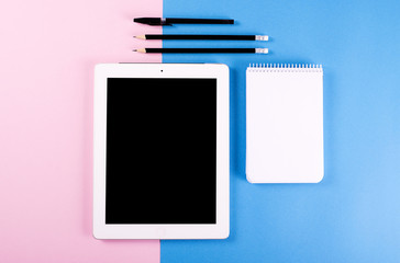 Computer keyboard next to tablet and pencils and a ballpoint pen on pink and blue background. Technology.
