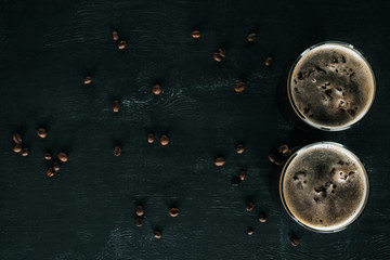 top view of glasses of cold brewed coffee with ice on dark surface with roasted coffee beans around