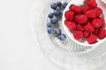 fresh raspberries in a white cup on a glass plate isolated
