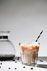 close up view of glass of cold brewed coffee with straw, coffee maker and roasted coffee beans on grey background