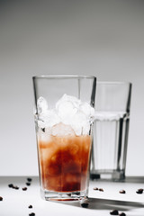 close up view of glass of cold brewed coffee with ice cubes and roasted coffee beans on grey background