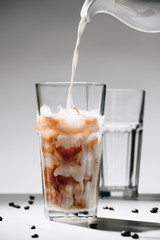 close up view of pouring milk into glass of iced coffee process on grey backdrop