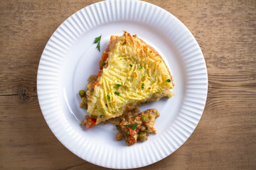 Classic homemade shepherd's pie (mashed potato and ground beef with vegetables) in white plate on wooden table. overhead, horizontal
