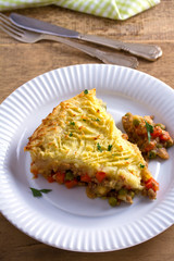 Classic homemade shepherd's pie (mashed potato and ground beef with vegetables) in white plate on wooden table. vertical