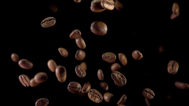 Fried coffee beans fly to the camera on a dark background. Slow motion