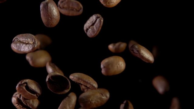 Fried coffee beans bouncing against to the camera on a dark background. Slow-motion shooting, very close-up