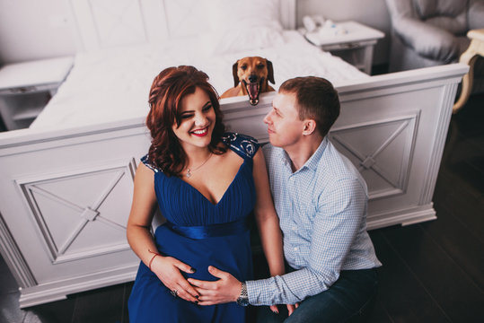 Young family, pregnant woman and her partner or husband with dog sitting on floor
